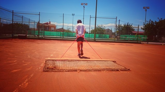 Ni&ntilde;o pasando la estera por pista de tenis de tierra batida