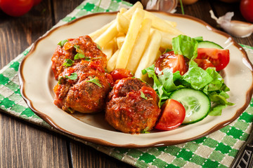 Roasted meatballs in tomato sauce with french fries and salad