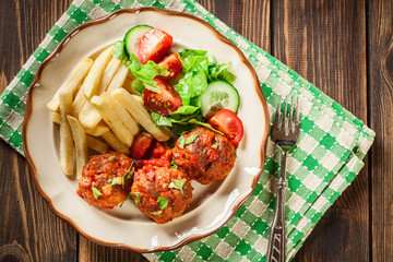 Roasted meatballs in tomato sauce with french fries and salad