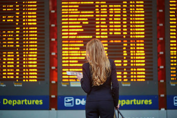 Woman with hand luggage in international airport terminal, looking at information board