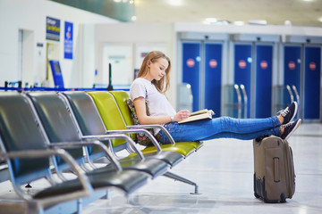 Young travelerin international airport reading a book while waiting for her flight