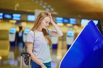 Unhappy tourist girl in international airport, doing self check-in
