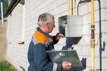A gray-haired master specialist man repairs a gas meter hanging on a brick wall. Maintenance of gas...