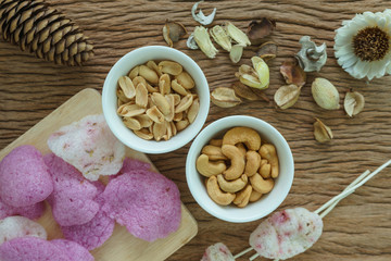 Roasted cashew nuts and peanuts with magenta crisp rice crackers appetizer in white bowl on wooden table