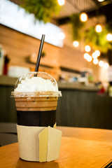 Iced coffee in takeaway cup on wood table with blurred coffee cafe background, selective focus