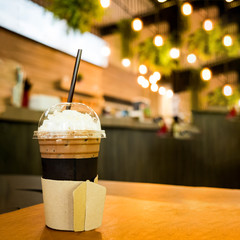 Iced coffee in takeaway cup on wood table with blurred coffee cafe background, selective focus