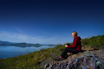 Fototapeta premium A lake with a gentle rocky shore at night. The girl is sitting on the lake.