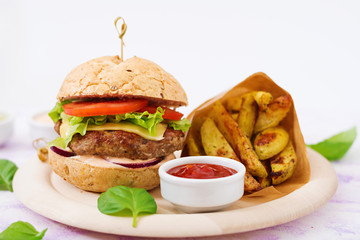 Big sandwich - hamburger with juicy beef burger, cheese, tomato, and red onion on light background and French fries.