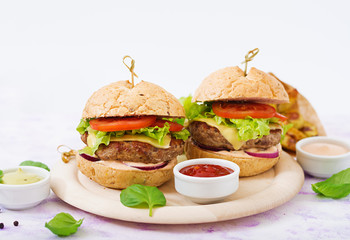 Big sandwich - hamburger with juicy beef burger, cheese, tomato, and red onion on light background and French fries.