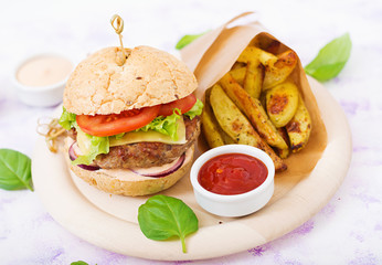 Big sandwich - hamburger with juicy beef burger, cheese, tomato, and red onion on light background and French fries.