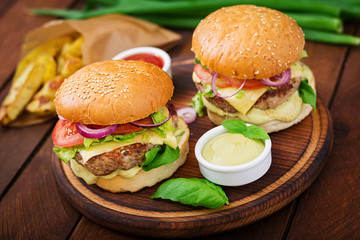 Big sandwich - hamburger with juicy beef burger, cheese, tomato,  and red onion on wooden background