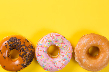 Three different donuts on yellow background. Top view and free space for text