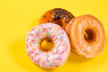 Three different donuts on yellow background. Close up image with selective focus