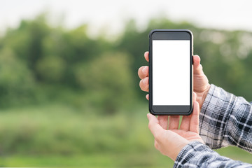 man holding smartphone in hands against green spring background 
A Man using his Mobile Phone outdoor, blank screen close up shot.