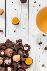 Raw handmade chocolate candies, cup of tea on white wooden background. Healthy breakfast with vegan sweets. Top view