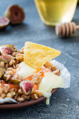 Melted baked French soft cheese from Brittany region covered with chopped figs, walnuts and honey on dark background. Snack concept with chips. Selective focus