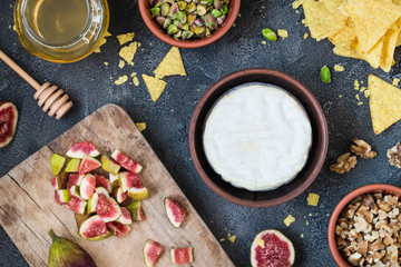 Ingredients layout for baking soft cheese brie with figs, walnuts, pistachios and honey. Snack concept with chips. Top view on dark background