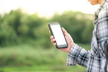 man holding smartphone in hands against green spring background 
A Man using his Mobile Phone outdoor, blank screen close up shot.