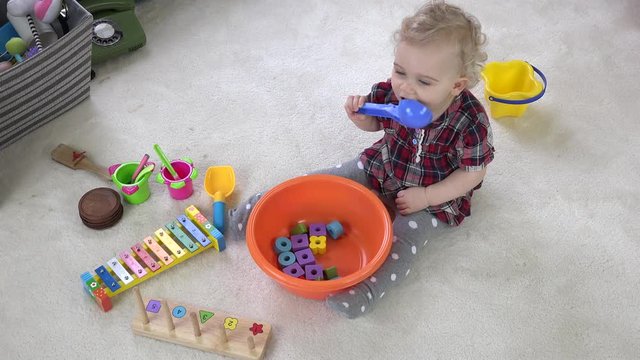 Baby girl mix wooden bricks in bowl with big spoon. Cooking imitation with toys