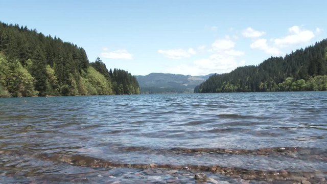 Water approaches camera from low angle on small stone shore of fresh alpine lake in the Pacific Northwest wilderness.