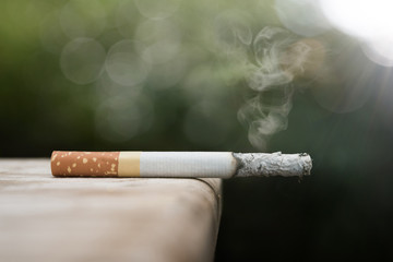 Close up cigarette burning on wood floor and green bokeh blur background , stop quitting tobacco...