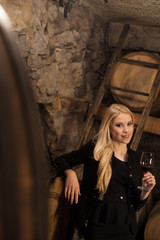 Beautiful young blond woman drinks wine in wine cellar