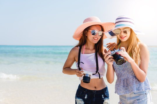 Two cool trendy hipster girls at the beach enjoying vacation on a tropical island, perfect tanned body, healthy skin, sexy stylish casual wear, bikini, blonde and brunette with the camera, sunglasses