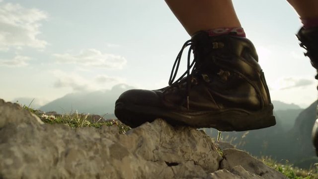 CLOSE UP SLOW MOTION LOW ANGLE Unrecognizable person in mountaineering boots walking down the steep rocky footpath in sunny mountain. Woman in hiking boots on outdoor adventure exploring stunning Alps