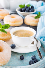 Cup of coffee and homemade donuts with powdered sugar and fresh blueberries on light gray background. Selective focus.