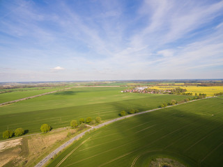 
Aerial view of green agricultural fields with a country road and a smal city under blue sky in germany
