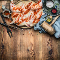 Whole chicken flattened out with condiment and kitchen tools on wooden rustic background, cooking preparation , top view. Chicken Tabaka traditional Georgian dish , Caucasian cuisine