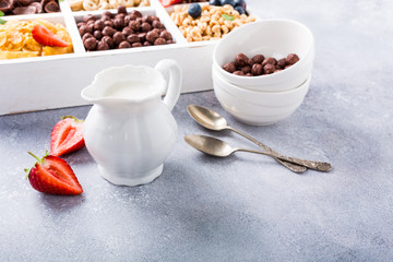 Milk jug and variety of cold quick breakfast cereals with berries in white wooden box, healthy eating concept, selective focus, copy space.