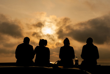Four people are sitting on the background of the sea at sunset