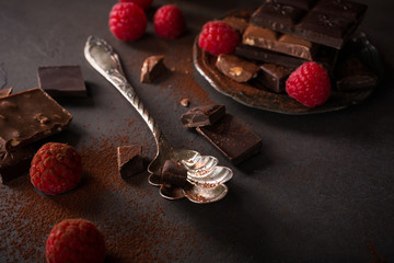 Broken chocolate pieces and raspberries on brown background with copy space. Dark photo.