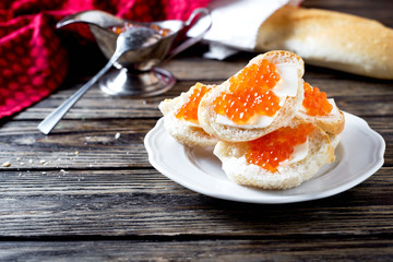 Snack, sandwiches with butter, red caviar, crispy baguette and white wine on a wooden background 