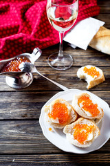 Snack, sandwiches with butter, red caviar, crispy baguette and white wine on a wooden background 