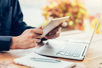 Asia man using tablet and laptop on table in coffee shop with vintage toned filter.
