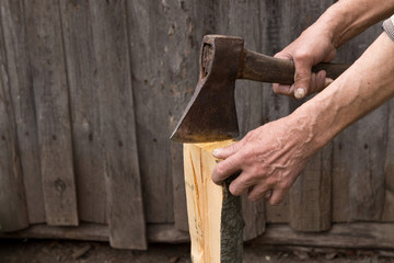 Worker, an elderly man with an old axe chops firewood. Forced to work in retirement . Employee .