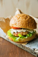Close-up photo of home made hamburger with beef, onion, tomato, lettuce, cheese and spices. Fresh burger closeup on wooden rustic table with potato fries and chips.