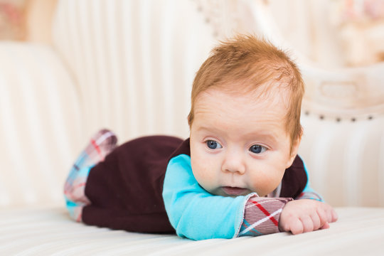 Close-up portrait of baby boy with red hair and blue eyes. Newborn child lyling in couch.