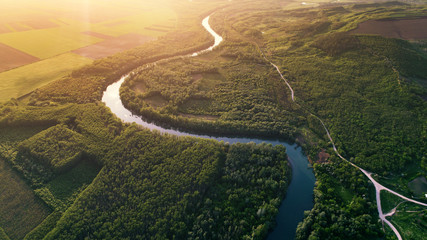 Winding river and green banks shot at sunset from drone
