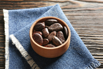 Bowl with aromatic cocoa beans on wooden background