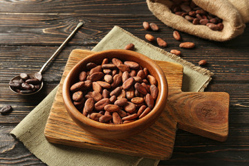 Bowl with aromatic cocoa beans on wooden background