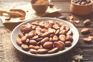 Plate with aromatic cocoa beans on wooden table