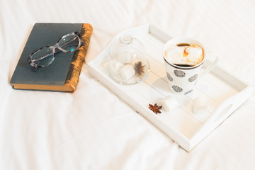 Breakfast in bed - tray with cup of coffee and marshmallows, book and glasses, cozy hygge home style