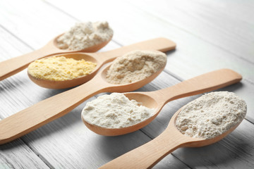 Spoons with different types of flour on light wooden background, closeup