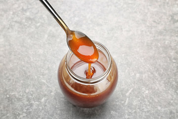 Jar with tasty caramel sauce and spoon on light background