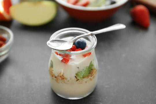 Glass jar with tasty yogurt, berries and spoon on table