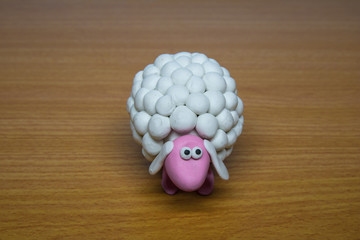 A single white polymer clay cute sheep on a wooden background