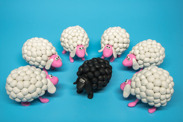 Concept - A circle of white sheep surrounds one black sheep, on a solid blue background. 